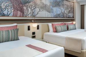 Doppelzimmer im Delphin Palace Hotel mit zwei Betten, Sofa, Schreibtisch und Terrassentür.