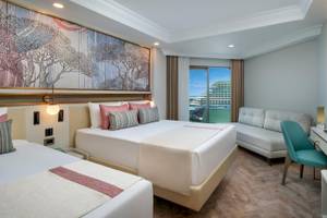 Doppelzimmer im Delphin Palast Hotel mit zwei Betten, Sofa und großer Fensterfront.