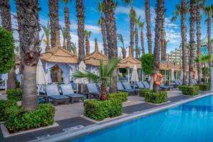 Außenbereich des Delphin Palace Hotels mit Swimmingpool, Liegestühlen und Palmen.