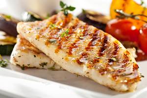 Zwei Stücke gebratener Fisch auf einem weißen Teller mit Gewürzen und Gemüse.