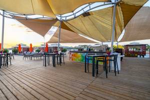 Terrasse des VONRESORT Golden Coast mit Tischen, Stühlen und Sonnenschirmen bei Sonnenuntergang.