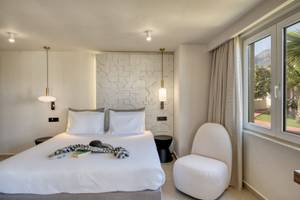 Georgioupolis Resort Aquapark & SPA Zimmer mit Bett, weißem Stuhl und Fenster mit Aussicht auf den Berg.