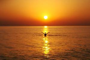 Eine Person schwimmt im Meer während des Sonnenuntergangs, mit der Sonne, die auf dem Horizont untergeht.