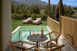 Terrasse im Georgioupolis Resort Aquapark & SPA mit Blick auf einen Swimmingpool, Liegen und Weinflasche.