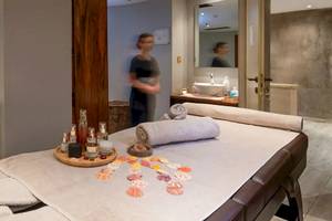 Massagebehandlungsraum im Cactus Village Hotel mit zwei Liegen, einer offenen Tür und einer Frau im Hintergrund.