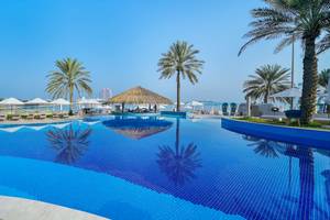 Poolbereich des Radisson Blu Hotel & Resort am Abu Dhabi Corniche mit Sonnenliegen und Palmen