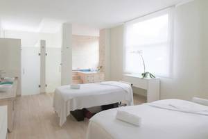 Spa-Behandlungsraum im Hotel JOIA Bávaro by Iberostar mit zwei weißen Behandlungsliegen und einem Whirlpool im Hintergrund.