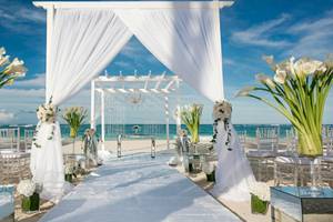 Strandhochzeitszeremonie im JOIA Bávaro by Iberostar mit weißen Vorhängen und Blumen.