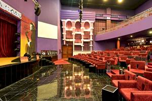 Ein Kinosaal mit leeren roten Stühlen, roter Teppich, und rote Vorhänge.