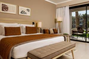 Ein Schlafzimmer mit einem Bett, Kissen, einem Couch, einem Tisch und einer Terrasse im Jaz Elite Amara Hotel