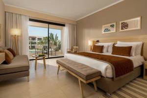 Hotelzimmer des Jaz Elite Amara mit großem Bett, Sofa, Tisch und Blick auf einen Swimmingpool.