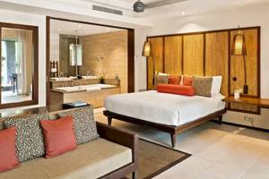 Innenansicht eines Schlafzimmers im Constance Ephelia Resort mit großem Bett, Sofa, Badewanne und Dekor.