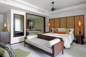 Innenansicht des Schlafzimmers im Constance Ephelia Resort mit Bett, Sofa, Spiegeln und Lampen.