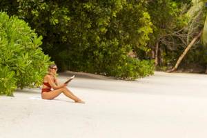 Frau sitzt am Strand im Constance Ephelia Resort und liest ein Buch.