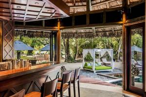 Innenansicht der Bar und Loungebereich des Constance Ephelia Resorts mit grüner Bettlandschaft und Sonnenschirmen.