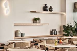 Restaurantbereich des Atlantica Beach Resort Kos mit Esstischen und Vasen auf Regalen.