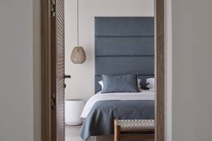 Zimmer im Atlantica Beach Resort Kos mit einem Bett, blauem Kopfteil und einem weißen Stuhl.