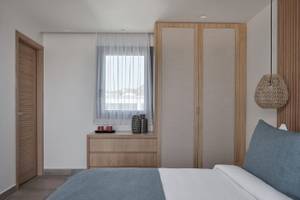 Inneneinrichtung eines Schlafzimmers im Atlantica Beach Resort Kos mit Doppelbett, Nachttisch, Kleiderschrank und Fenster mit Vorhängen.