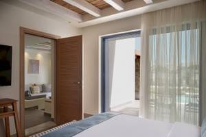 Innenansicht eines Zimmers im Atlantica Beach Resort Kos mit offenem Eingang, offenem Balkon, Bett, Fernseher und Blick auf den Pool.