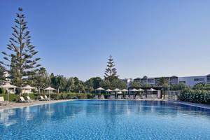 Außenpoolbereich des Atlantica Beach Resort Kos mit weißen Liegestühlen und Sonnenschirmen.