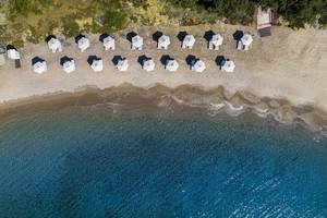 Luftaufnahme des Atlantica Beach Resort Kos mit vielen weißen Sonnenschirmen am Strand und blauem Meer.