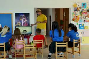 Hotelmitarbeiter zeigt Kindern einen Film auf dem Monitor im Klassenzimmer.