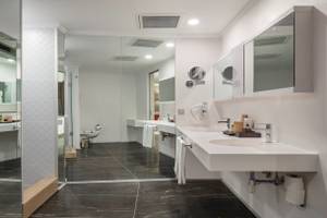 Das Badezimmer des Nirvana Cosmopolitan Hotels mit weißen Waschbecken und schwarzen Marmorboden.