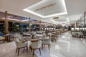 Innenbereich des Nirvana Cosmopolitan Hotels mit vielen Tischen und Stühlen, hängenden Kronleuchtern und großen Fenstern.