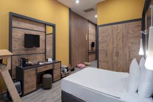 Hotelzimmer im Nirvana Cosmopolitan mit gelben Wänden, Holzelementen, einem Fernseher, Schreibtisch, Bett und Katzenzubehör.