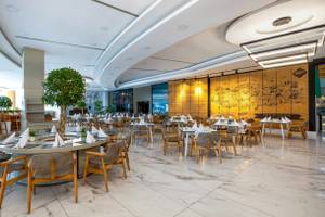 Innenbereich des Nirvana Cosmopolitan Hotels mit gerundeten Tischen, Holzstühlen und weißer Marmorfliesen.