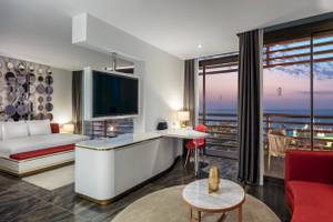 Innenansicht des Nirvana Cosmopolitan Hotels mit Bett, Schreibtisch und Aussicht auf den Ozean.