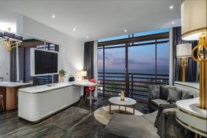 Modernes Hotelzimmer mit Meerblick, Tisch, Stühlen, Sofa, Fernseher und Lampen.