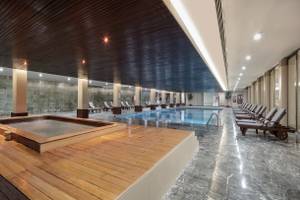 Innenpoolbereich des Nirvana Cosmopolitan Hotels mit Holzboden, Sitzliegen und einer großen Poolfläche.