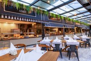 Speisebereich des Nirvana Cosmopolitan Hotels mit Tischen, Stühlen und Pflanzendekoration.