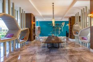 Innenansicht des Nirvana Cosmopolitan Hotels, zeigt einen großen Loungebereich mit einem Tisch und Sesseln, umgeben von blauen Wänden und modernen Möbeln.