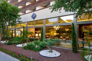 Außenansicht des Nirvana Cosmopolitan Hotels mit Garten, Bäumen und Glasfassade.