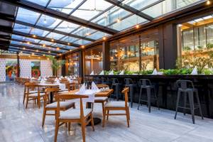 Innenbereich des Nirvana Cosmopolitan Hotels mit Glasdach, Tischen, Stühlen und Pflanzen.