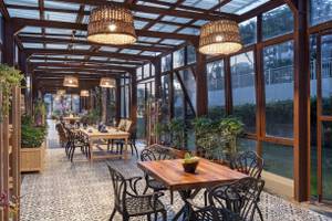 Innenansicht der Terrasse des Nirvana Cosmopolitan Hotels mit Tischen, Stühlen und Pflanzen.