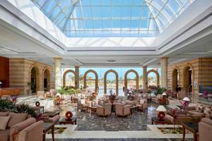 Lobby des Jaz Grand Marsa Hotels mit Glasdach und vielen Sitzgelegenheiten.