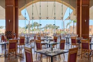 Restaurantbereich im Jaz Grand Marsa Hotel mit Glaswänden und Blick auf Palmen.