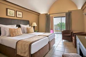 Doppelzimmer im Jaz Lamaya Resort mit zwei Betten, Sessel, Schreibtisch und Balkon mit Meerblick.