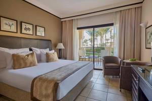 Schlafzimmer im Jaz Lamaya Resort mit einem großen Bett, Kissen und einem Balkon mit Blick auf Palmen.