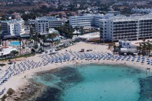 Luftaufnahme des Anonymous Beach Hotels mit vielen Gästen und blauen Sonnenschirmen am Strand.