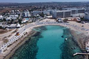 Luftaufnahme des Anonymous Beach Hotels, das an einen Strand angrenzt mit vielen Sonnenliegen und blauem Wasser.