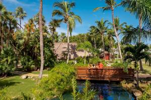 Familie auf einer Brücke im Sunscape Dominicus La Romana Hotel, umgeben von Palmen und Wasser.