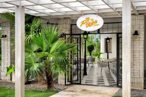 Eingang zum Hotel-Restaurant mit Palmenbaum und schwarzen Gittertüren.