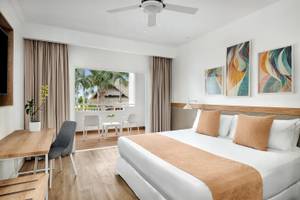 Innenansicht eines Hotelzimmers im Sunscape Dominicus La Romana mit einem Bett, Tisch, Stühlen und einer Terrassentür.