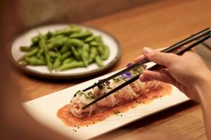 Asiatisches Gericht mit Sushi-Nudeln, rotem Dip und grünen Bohnen auf einem weißen Teller.