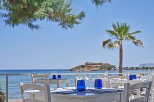 Terrasse des Atlantica Kalliston Resorts mit Tischen und Blick auf das Meer.