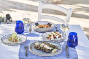 Mehrere Gerichte und Gläser Wein auf einem Tisch im Freien im Atlantica Kalliston Resort.